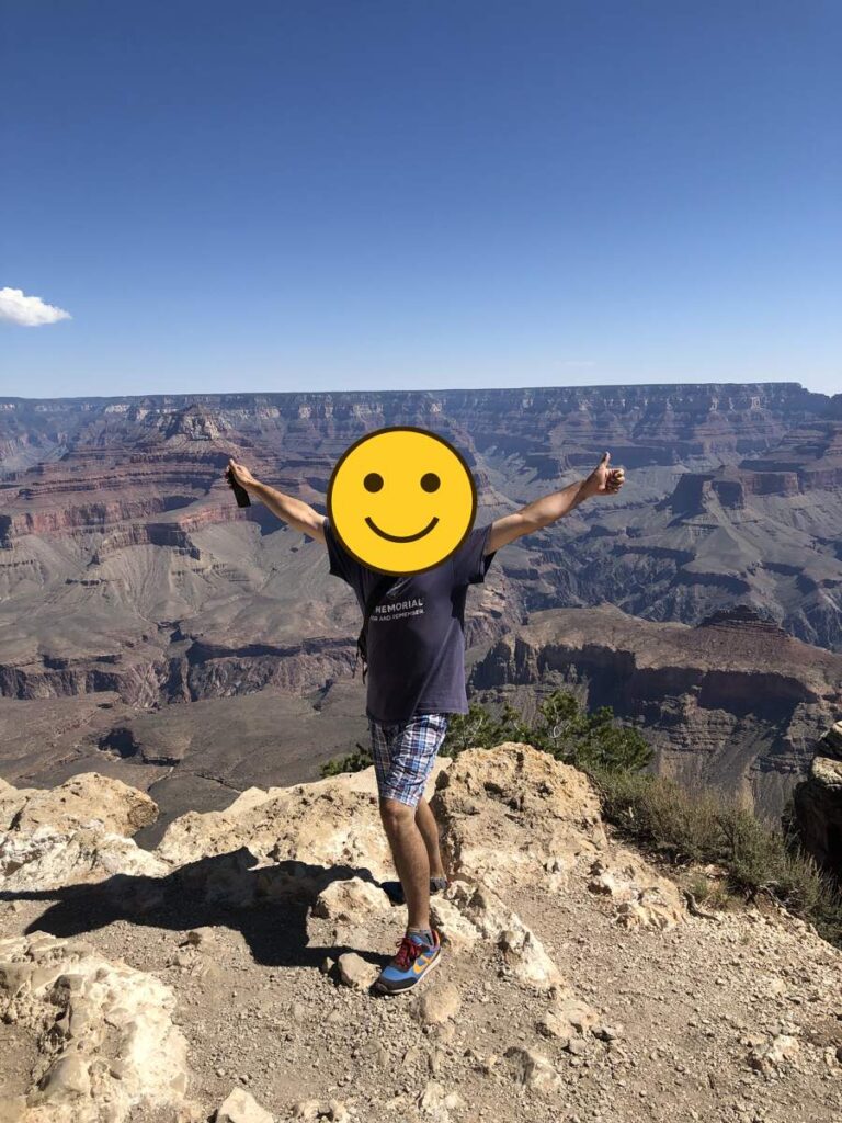 グランドキャニオンの断崖を背景に、両手を広げて立つ旅行者