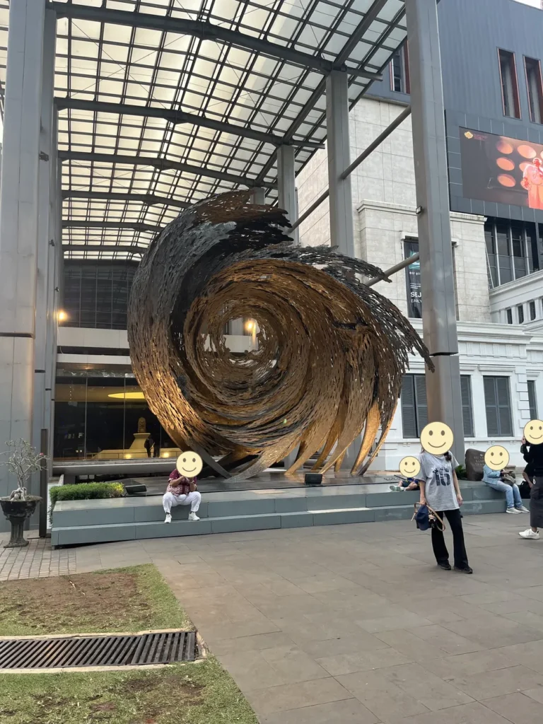 国立博物館の敷地にある、渦を巻いたような大きな金色のオブジェ。人の顔はニコちゃんマークで隠している