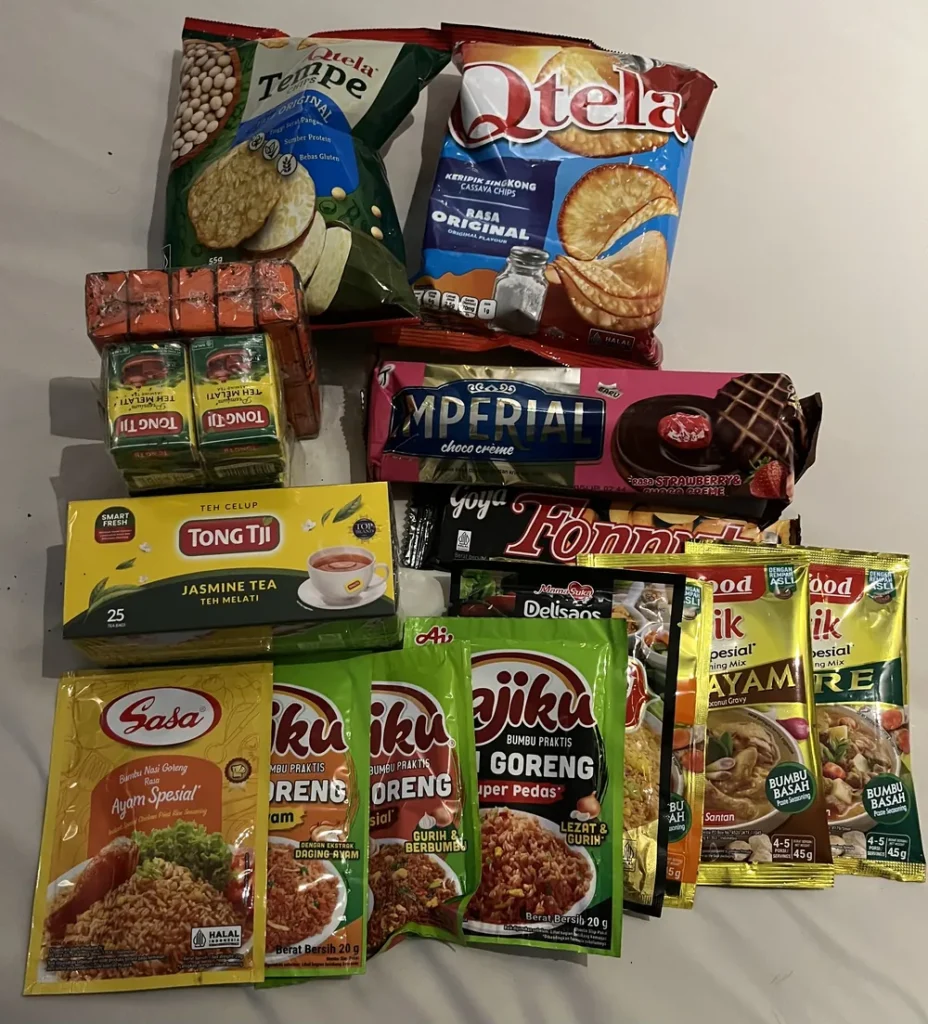 お土産に買ったインドネシアのお菓子とお茶。スナック菓子、ジャスミンティー、チョコレートのビスケット、ナシゴレンなどの調味料の袋が並んでいる