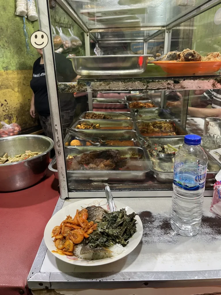 ホテル近くの食堂。ショーケースの前に、ご飯と、エビ・青菜・魚のおかずを盛った皿がある