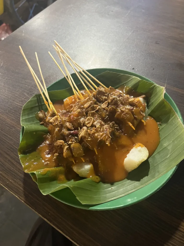 バナナの葉を敷いた皿に、串焼きととろみのあるソース、白いお餅のようなものがのっている